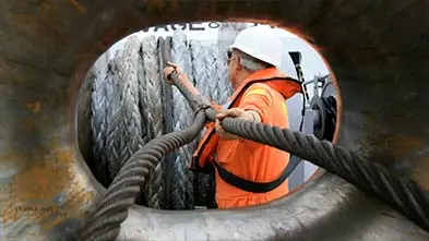Tugboat sailor feeding a heavy ship's mooring rope through the bow of the ship.